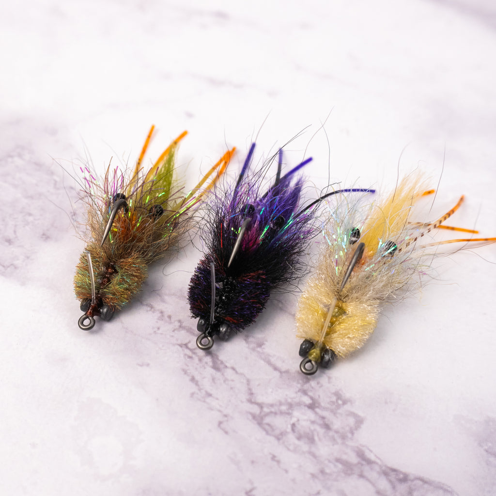 Three Bandit Crab saltwater fly patterns in olive, tan, and black purple colorways for redfish and inshore fly fishing.