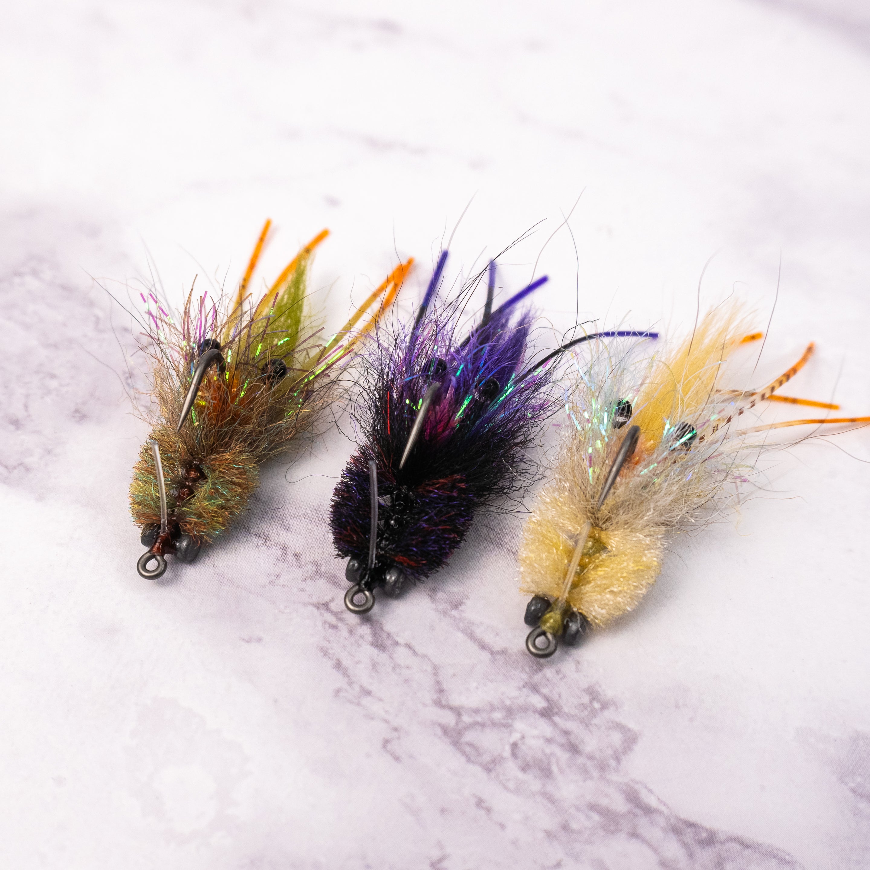 Three Bandit Crab saltwater fly patterns in olive, tan, and black purple colorways for redfish and inshore fly fishing.