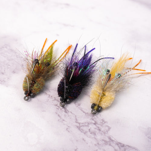 Three Bandit Crab saltwater fly patterns in olive, tan, and black purple colorways for redfish and inshore fly fishing.