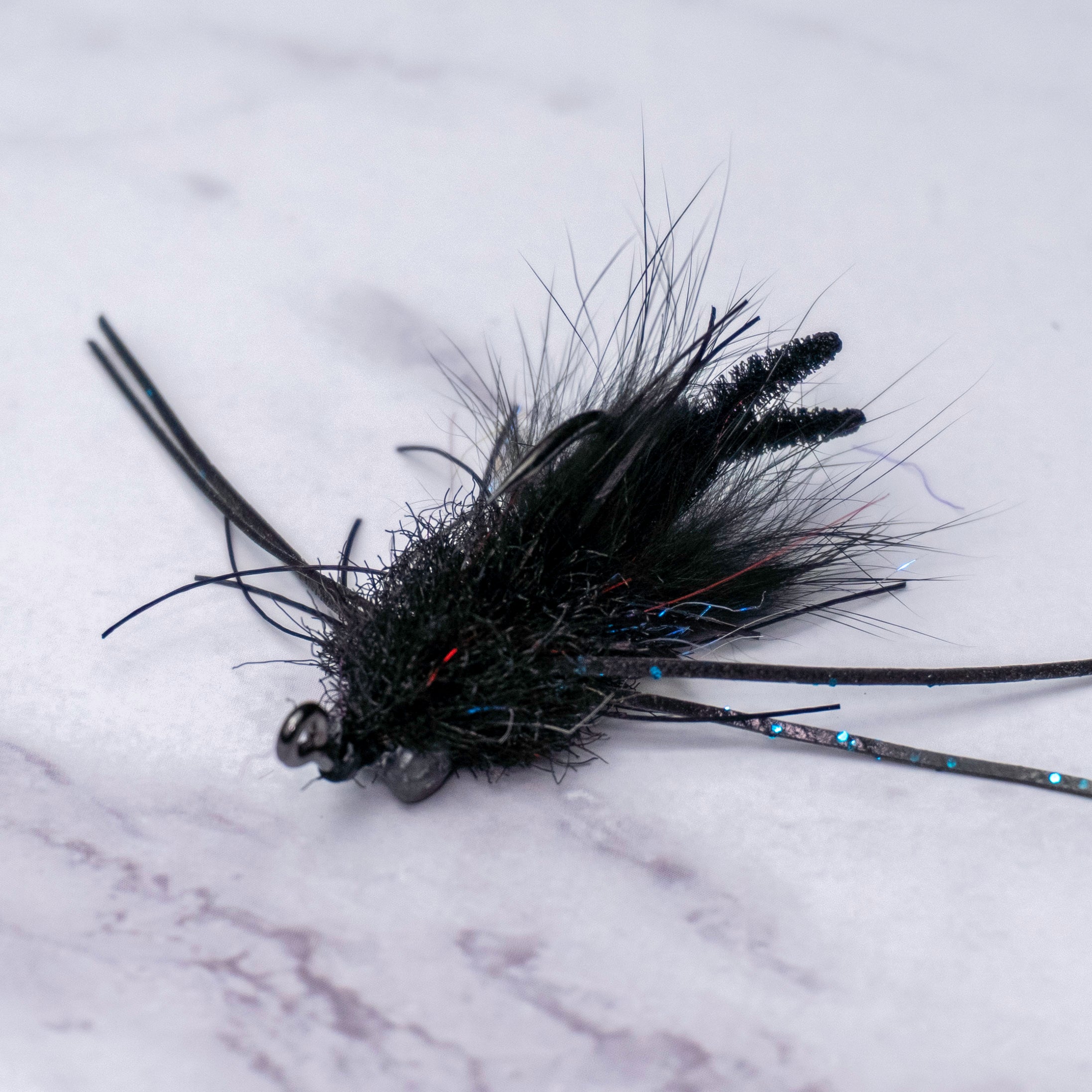 Macro view of Bourbon Crab fly in black colorway highlighting compact profile, silicone legs, and jig hook orientation