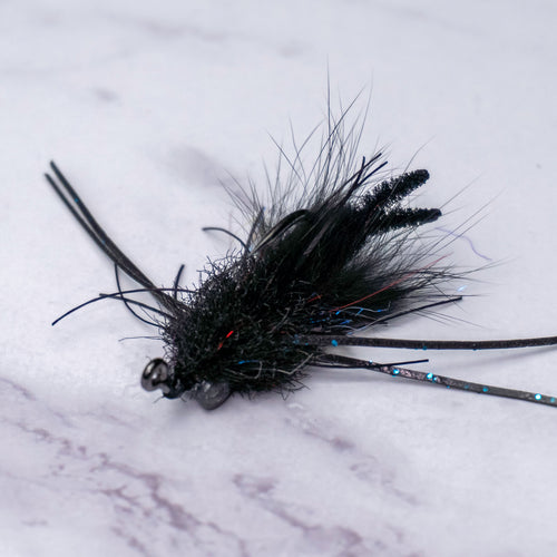 Macro view of Bourbon Crab fly in black colorway highlighting compact profile, silicone legs, and jig hook orientation