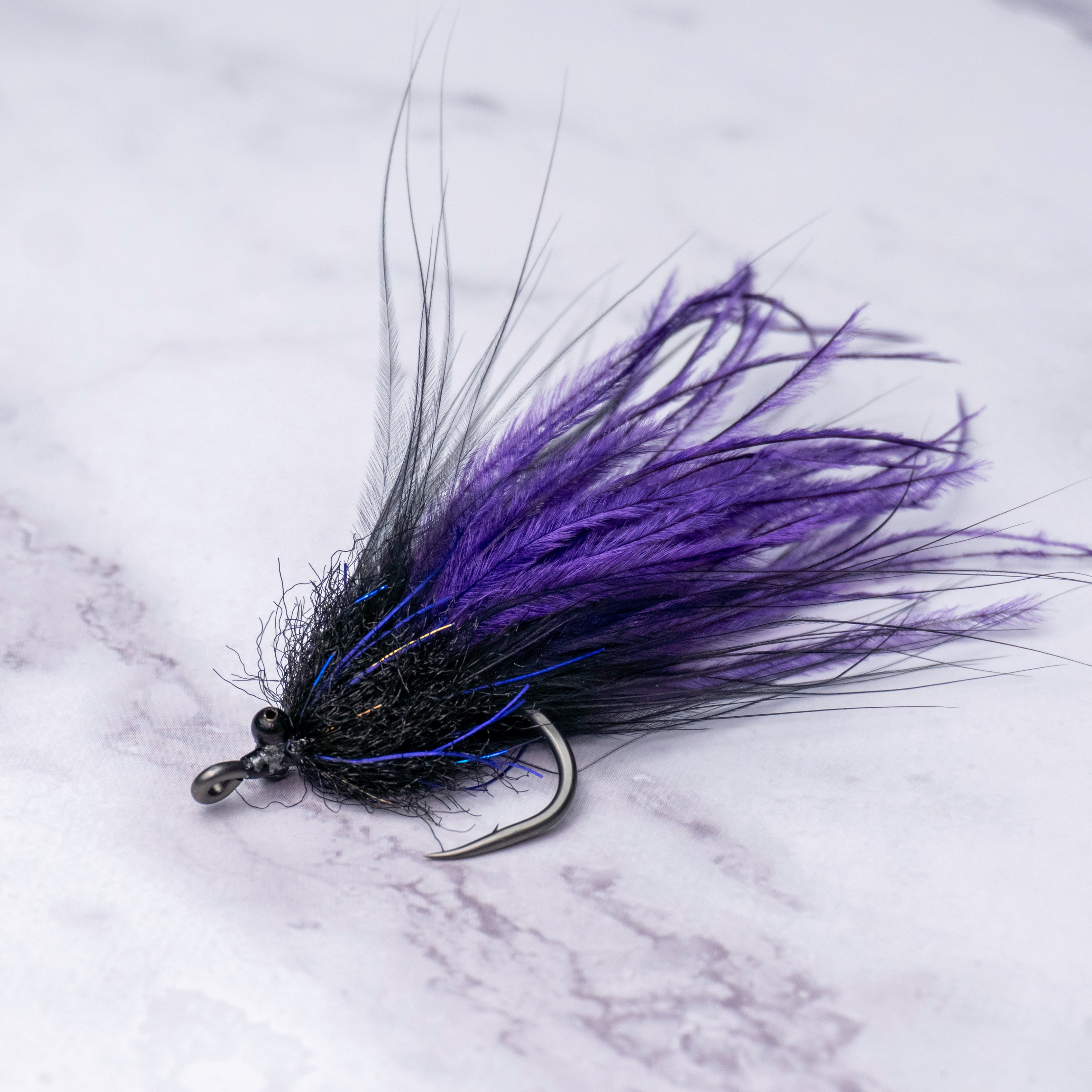 Black and purple Tickler tarpon fly with subtle flash accents, beach chain eyes, and a flowing suspended profile tied for backcountry tarpon, glades fish, and migrating summer fish.