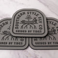 Gray 3.7 x 4 inch Southern Style Fly Co. Guided By Tides Skiff logo foam fly pad with adhesive backing for organizing saltwater and freshwater flies on boats, coolers, and fly boxes.
