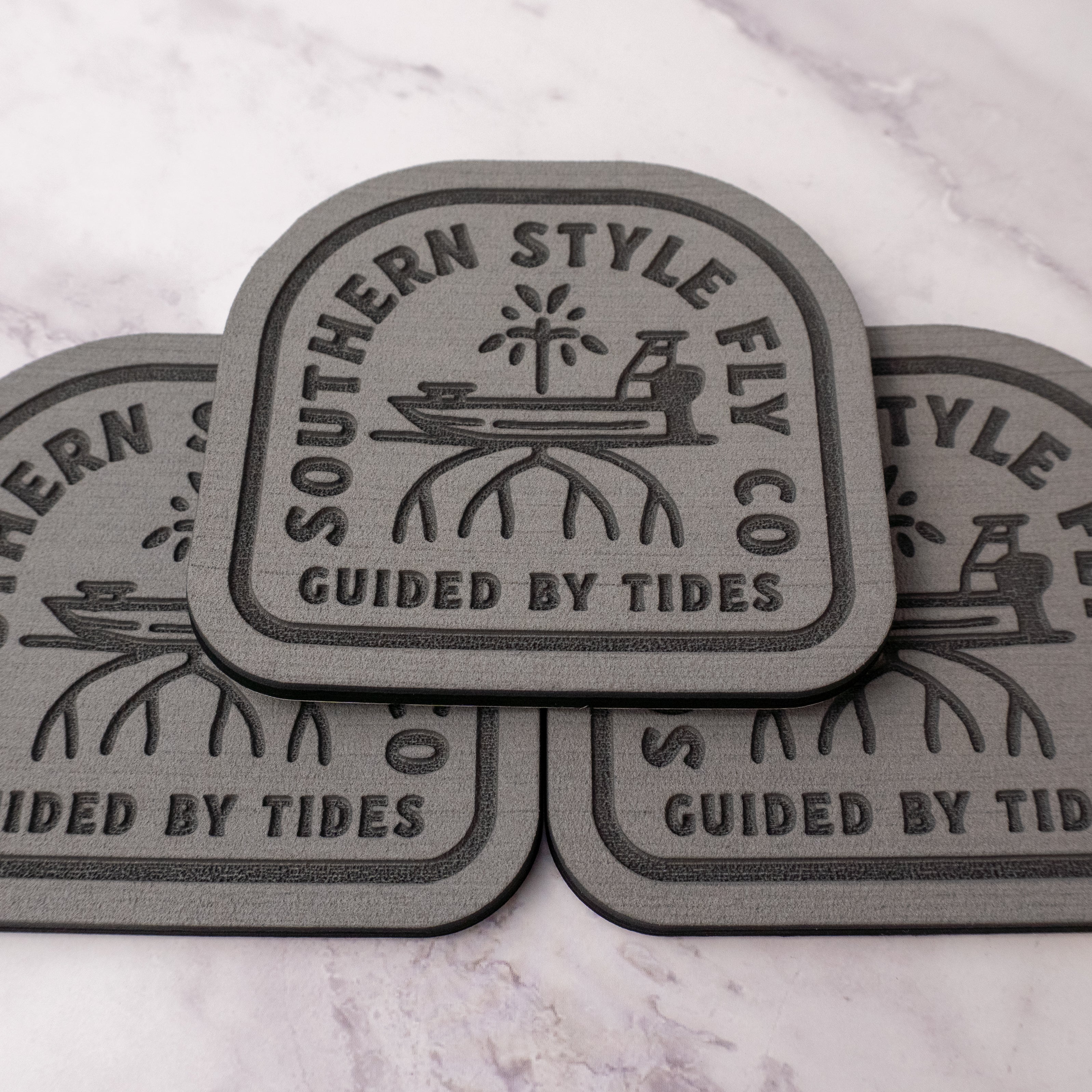 Gray 3.7 x 4 inch Southern Style Fly Co. Guided By Tides Skiff logo foam fly pad with adhesive backing for organizing saltwater and freshwater flies on boats, coolers, and fly boxes.