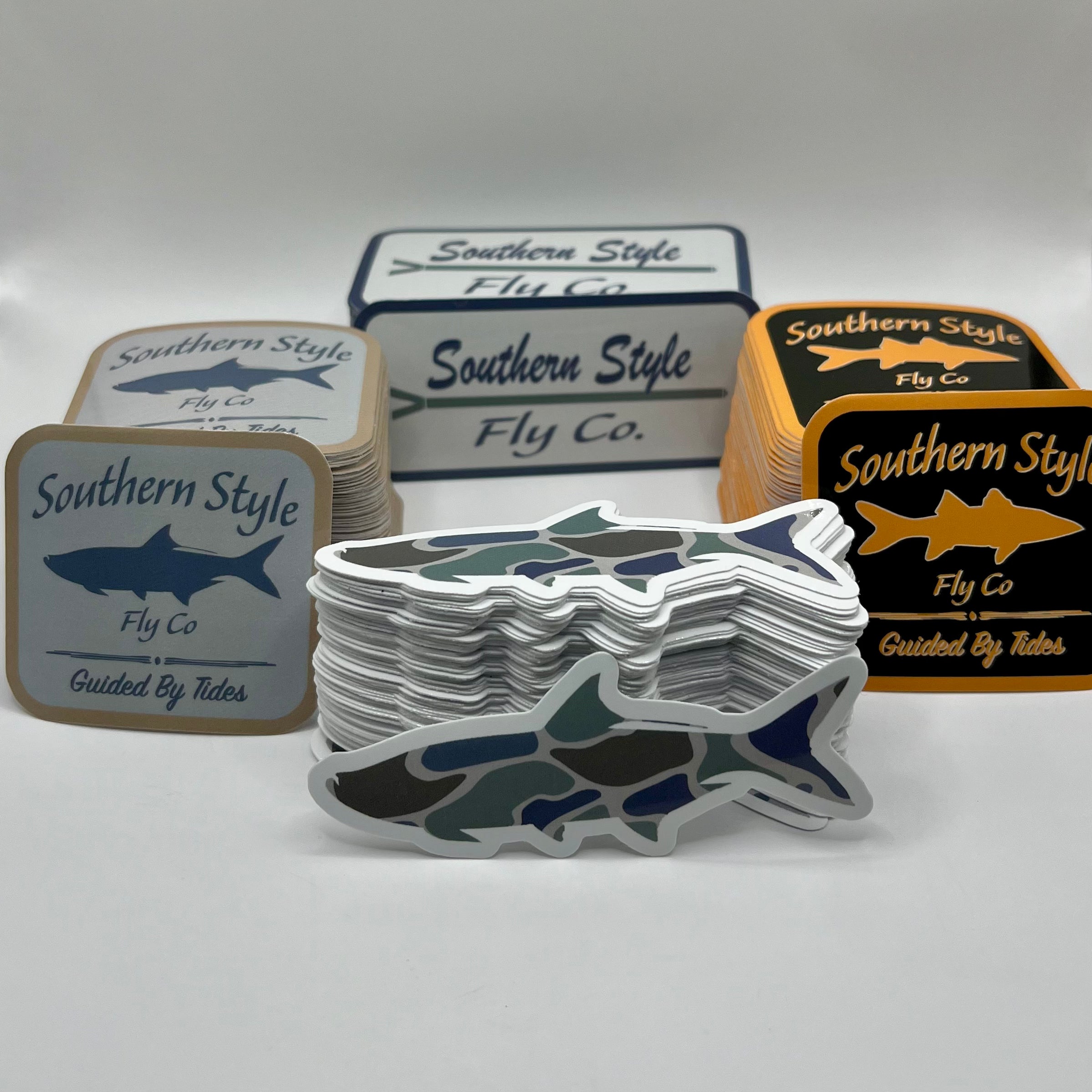 Assorted Southern Style Fly Co. fishing stickers displayed on a white background, including square logo stickers in multiple colorways and a stacked die-cut camo fish sticker in the foreground.
