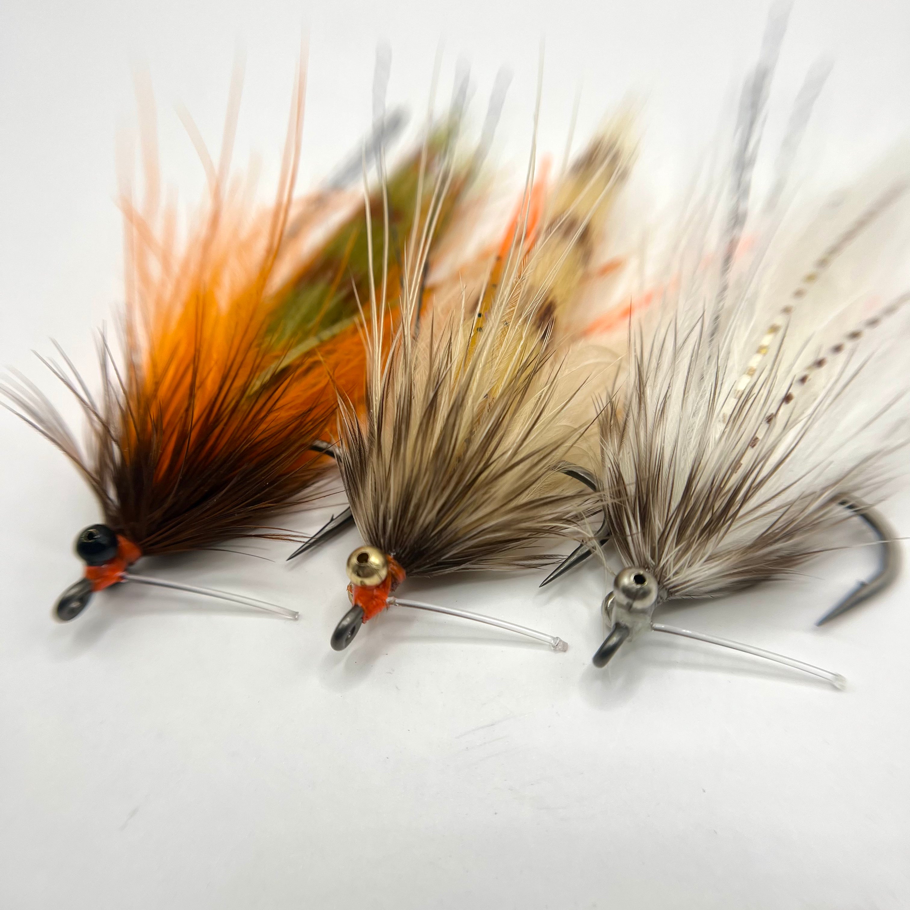 Macro image of the Stalker Shrimp fly showing all three color variations—white, tan, and orange-brown—highlighting lifelike legs, flowing materials, and movement-focused shrimp profile tied on a size 2 hook.