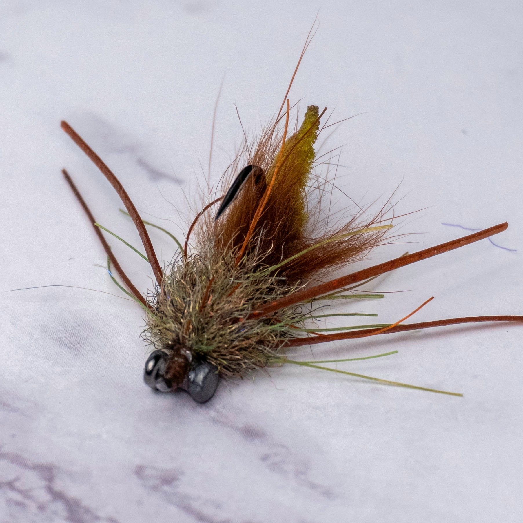 Muddy Olive Bourbon Crab saltwater fly pattern with a slim crab profile, olive and brown tones, rubber legs, and bead chain eyes tied for shallow water redfish and black drum.