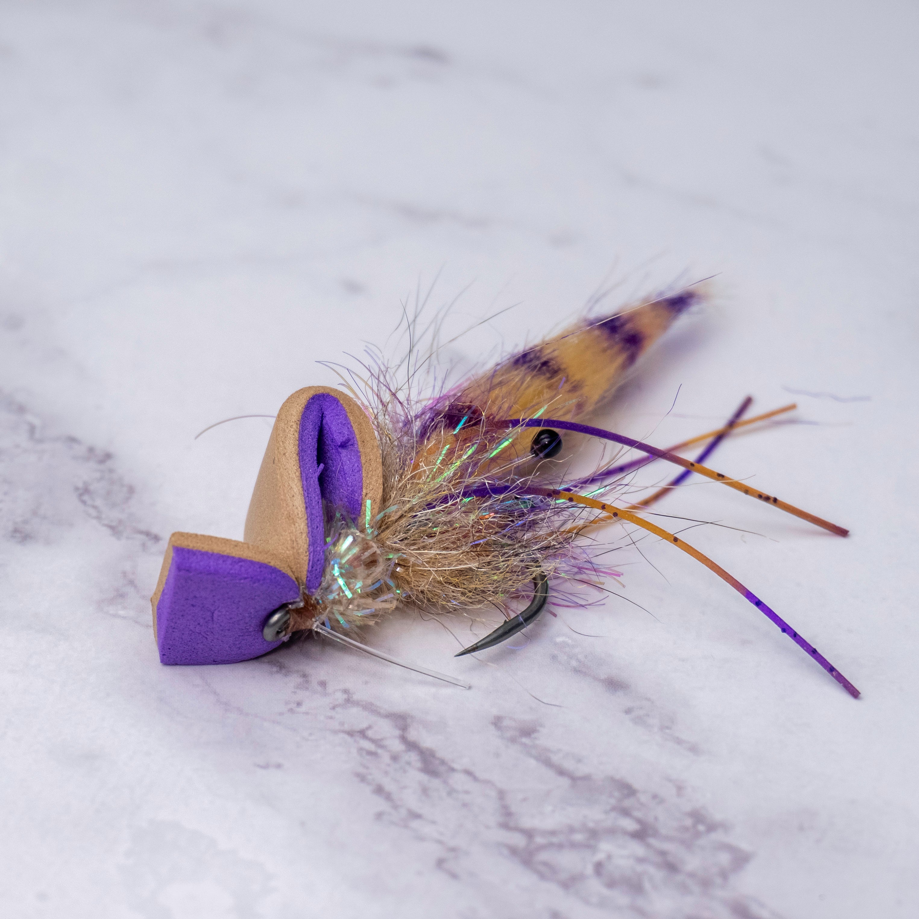 Limited batch Summer Collection Pop-N-Shrimp saltwater fly in purple and tan with popping foam head, barred tail, rubber legs, and flash materials on a white marble background.